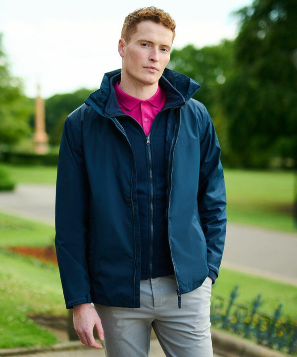 A person with short red hair is standing outdoors in a park, wearing a dark blue jacket by Regatta, RG059, over a pink polo shirt. The background shows greenery and a path.