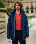 A man with curly hair wearing a navy blue Regatta RG108 over a red polo shirt stands outdoors in front of a historic building.