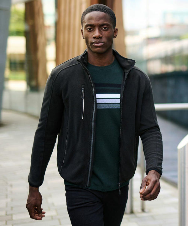 Man in a Regatta RG112 jacket and a dark green shirt with white and gray horizontal stripes walks outdoors on a paved pathway.