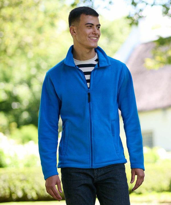 A person wearing a blue Regatta RG138 zip-up jacket and a striped shirt smiles while standing outdoors in a garden setting.