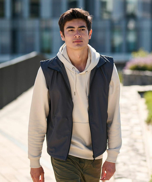 A person in a white hoodie and dark gray Regatta RG145 vest walks outdoors on a sunny day.
