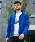 A person with curly hair wearing a blue **Regatta RG150** jacket and a white shirt walks outdoors near a modern building with a tree in the background.