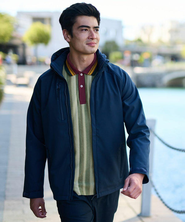 A man walking outdoors along a waterfront path, wearing a Regatta RG160 over a green and red polo shirt.