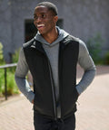 A man wearing a black Regatta RG164 vest over a gray hoodie is standing outside and smiling.