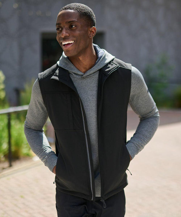 A man wearing a black Regatta RG164 vest over a gray hoodie is standing outside and smiling.