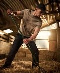Person in casual work attire uses a Regatta RG170 to move hay in a barn with sunlight streaming through wooden slats in the background.