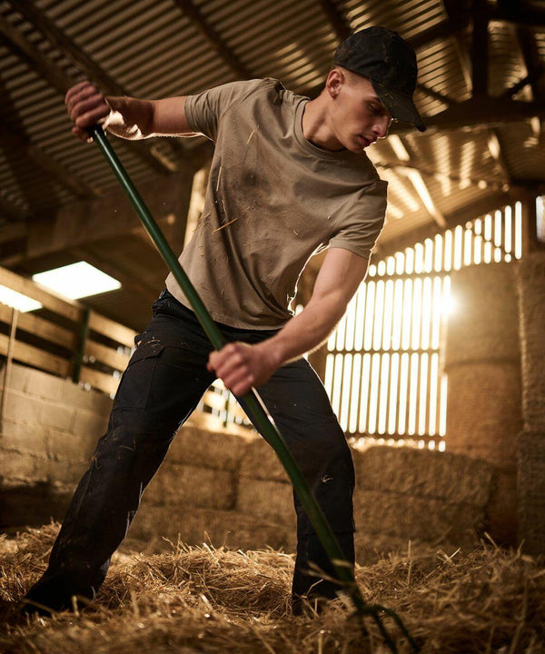 Person in casual work attire uses a Regatta RG170 to move hay in a barn with sunlight streaming through wooden slats in the background.