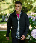 A young man wearing a black Regatta RG194 jacket and plaid shirt walks outdoors in a garden with hydrangeas and greenery in the background.