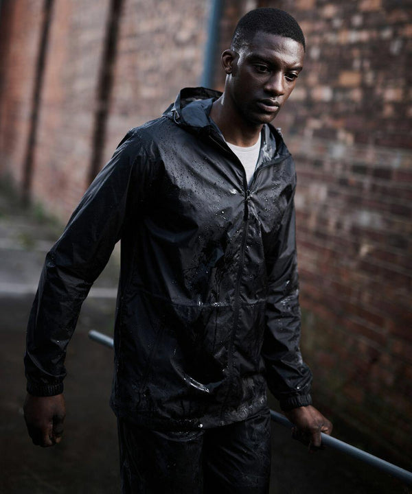A person in a black rain jacket walks outside near a brick wall on a wet day, holding a Regatta RG207.