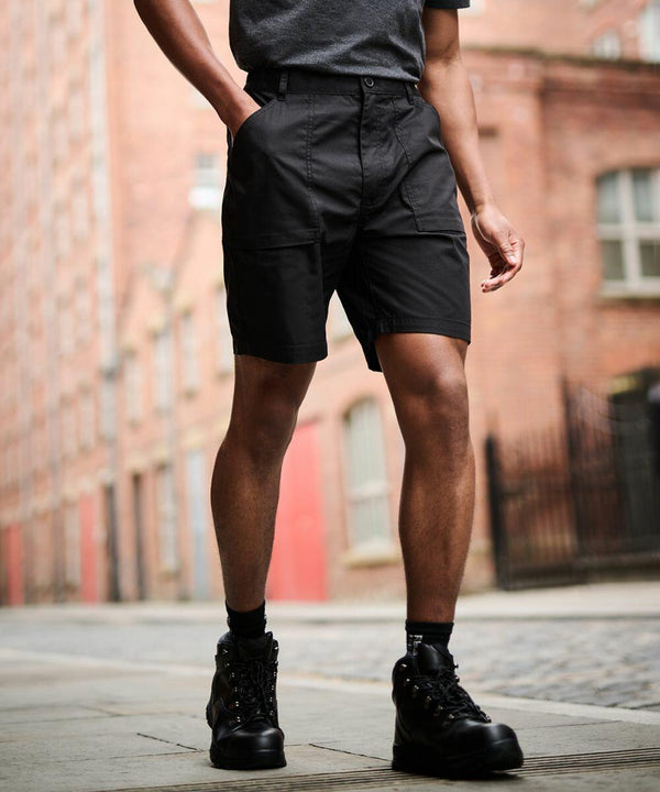 A person wearing a grey shirt, black shorts, and black Regatta RG234 boots stands on a paved street with hands in pockets, buildings visible in the background.