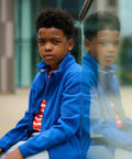 A boy in a Regatta RG248 jacket sits next to a glass wall, with his reflection visible in the glass.