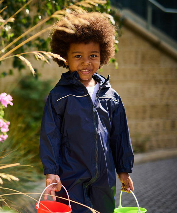 A child with curly hair, dressed in a navy blue raincoat, stands outdoors holding a green RG252 by Regatta in one hand and a red RG252 by Regatta in the other, smiling.