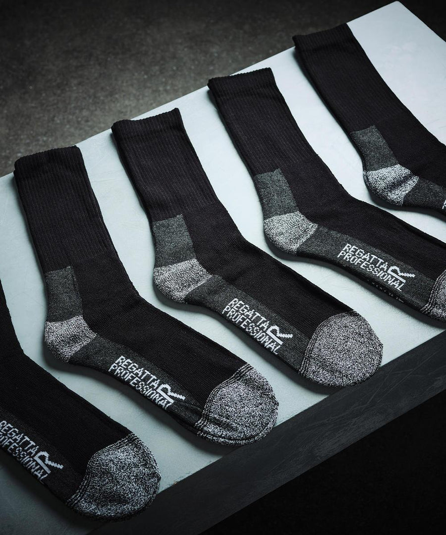 Five pairs from the Regatta Professional Pro 5-pack work socks, featuring reinforced heels and toes in black and grey, are laid out in a row on a grey surface with “REGATTA PROFESSIONAL” visible on each sole.