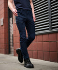 A person wearing dark blue cargo pants and black boots walks on a sidewalk next to a brick building with an RG307 Regatta metal vent.