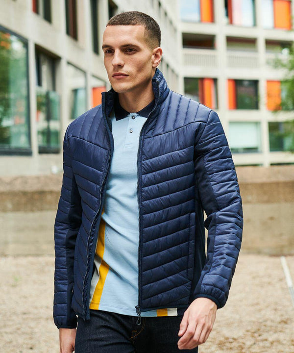 A person wearing a blue quilted Regatta RG319 and light blue shirt walks outside near a modern building with colorful window accents.