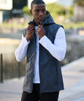 A person in a white long-sleeve shirt and gray Regatta RG320 stands outdoors, adjusting the RG320’s zipper, with a blurred urban background.