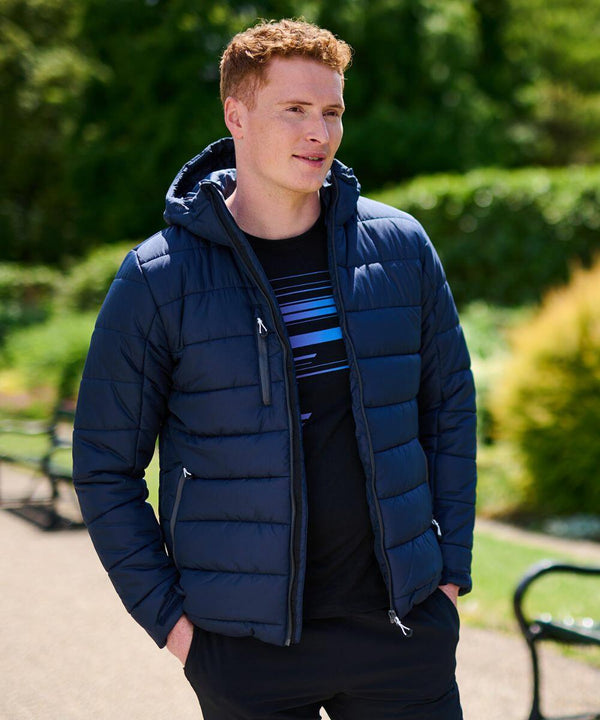 A person wearing a navy blue Regatta RG338 puffer jacket with a hood stands outdoors in a park, surrounded by greenery.