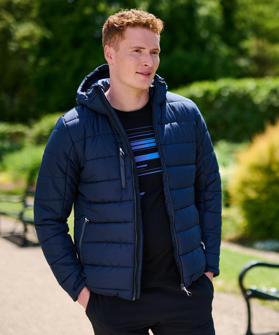 A person wearing a navy blue Regatta RG338 puffer jacket with a hood stands outdoors in a park, surrounded by greenery.