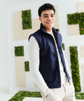 A man in a white long-sleeve shirt and dark blue RG351 by Regatta stands in front of a white wall decorated with green moss panels, smiling at the camera.