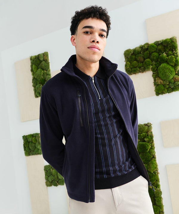 A person wearing a navy RG352 jacket and striped shirt stands in front of a white wall decorated with sections of green moss.