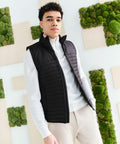 A person is standing in front of a wall decorated with moss and wooden panels, wearing a white shirt and a black RG357 vest from Regatta.