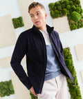A man wearing a navy **Regatta RG360** jacket, light blue and white polo shirt, and beige pants stands in front of a wall decorated with wooden panels and green moss.