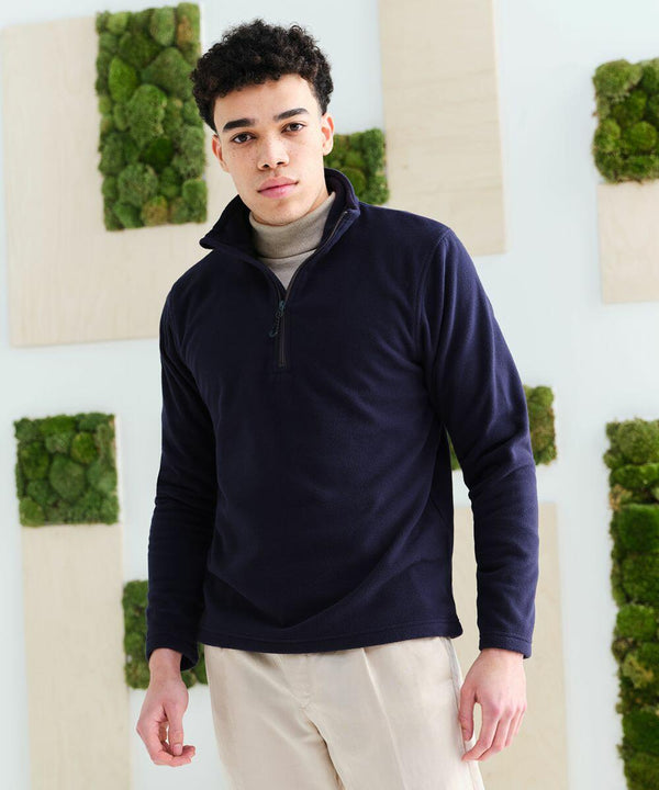 A person stands indoors wearing a navy blue RG362 zip-up sweater by Regatta and beige pants, with a backdrop of panels featuring green moss accents.