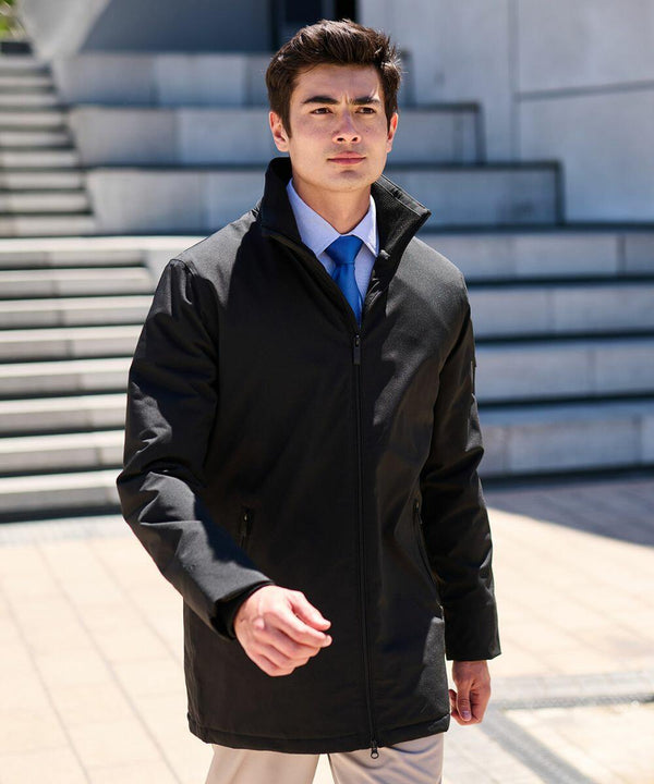 A man in a black RG364 by Regatta and blue tie walks outdoors in front of steps on a sunny day.