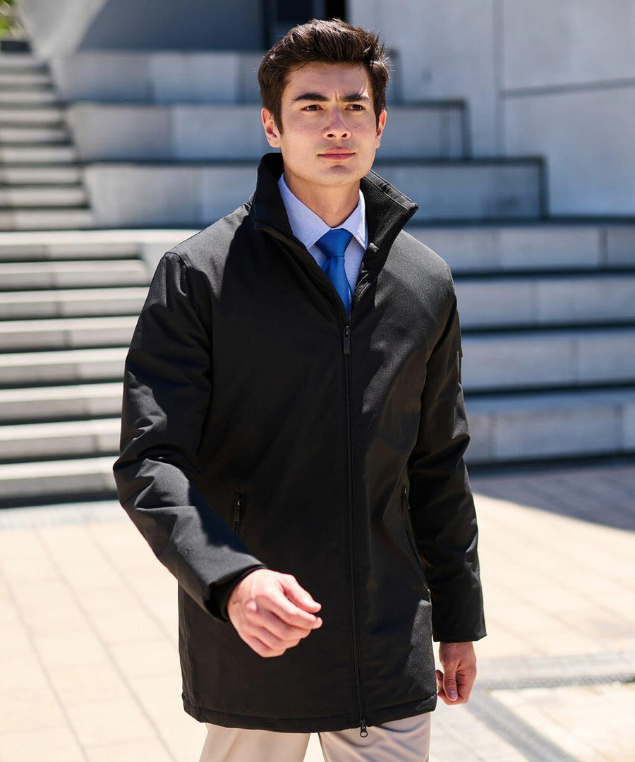 A man in a black RG364 by Regatta and blue tie walks outdoors in front of steps on a sunny day.