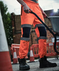 A person in an orange uniform with reflective stripes pushes a Regatta RG459 at a construction site, with traffic cones and barriers in the background.