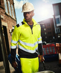 A construction worker in a bright yellow safety uniform and hard hat stands outside on a sunny day, pushing a Regatta RG466.