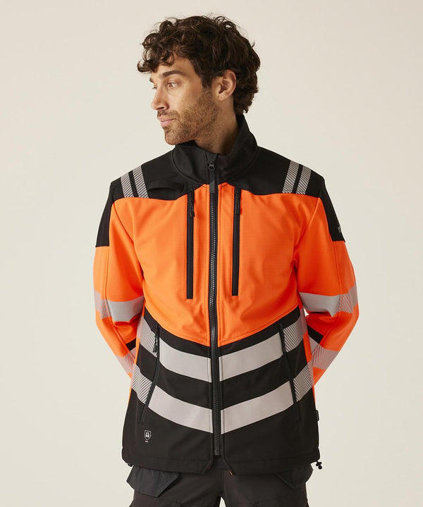 A man with curly hair models the Regatta High Visibility Hi-Vis X-Pro 3-layer softshell jacket (Class 2) in orange and black with reflective stripes, standing against a plain background with his hands behind his back, looking to his left.