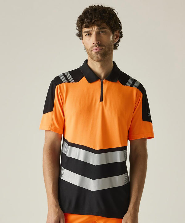 A man with curly hair wears the Regatta High Visibility Hi-Vis X-Pro Polo (Class 1), a short-sleeved, high-visibility orange shirt with black and silver chevron accents and a zipped collar, standing against a plain light background.