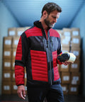 Man wearing a red and black jacket stands in a warehouse holding a roll of RG540 by Regatta, with cardboard boxes stacked in the background.