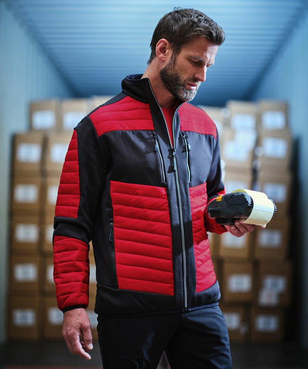 Man wearing a red and black jacket stands in a warehouse holding a roll of RG540 by Regatta, with cardboard boxes stacked in the background.