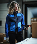 A woman in a blue and black jacket scans a cardboard box with a Regatta RG542 handheld barcode scanner in a warehouse.