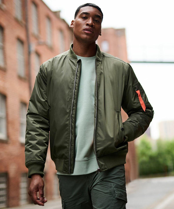 A man wearing a Regatta RG588 olive green bomber jacket and green pants stands in an urban alley with brick buildings.