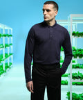 A person in a long-sleeve navy RG615 polo shirt by Regatta and black pants stands in an indoor garden with vertical shelves of plants.