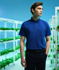 A person in a blue polo shirt stands in a Regatta RG616 hydroponic farm with rows of green plants on white shelves in the background.