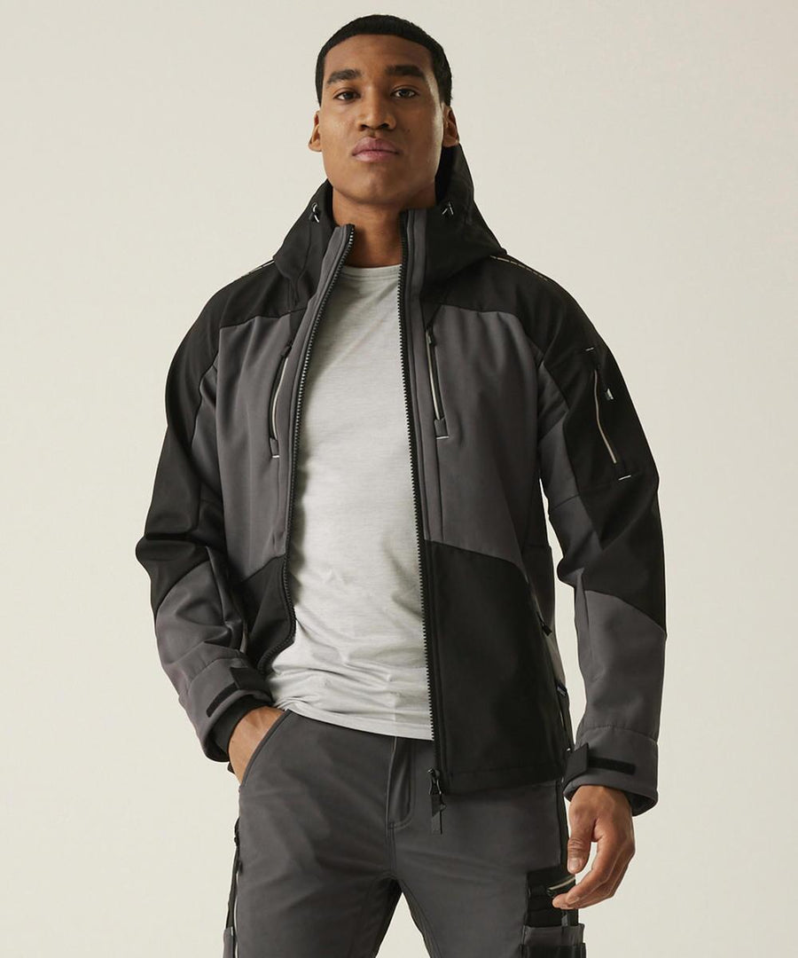 A man faces forwards, wearing the Regatta Professional 4-Tex stretch 3-layer softshell jacket in black and grey over a light grey T-shirt and matching grey trousers, against a plain light background.