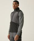 A person stands slightly to the side, wearing the Regatta Professional 4-Tex stretch 3-layer softshell bodywarmer in grey and black. The background is plain and light-coloured.