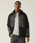 A man stands facing forwards, wearing the Regatta Professional 4-Tex stretch waterproof shell jacket over a light grey T-shirt and grey trousers. His hands are by his sides with a neutral expression, set against a plain, light background.