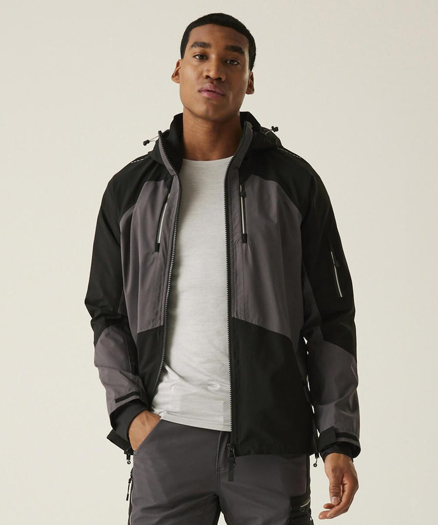 A man stands facing forwards, wearing the Regatta Professional 4-Tex stretch waterproof shell jacket over a light grey T-shirt and grey trousers. His hands are by his sides with a neutral expression, set against a plain, light background.