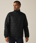 A person wearing the Regatta Professional Essential thermal jacket in black and dark jeans stands against a plain, light background, gazing off to the side.
