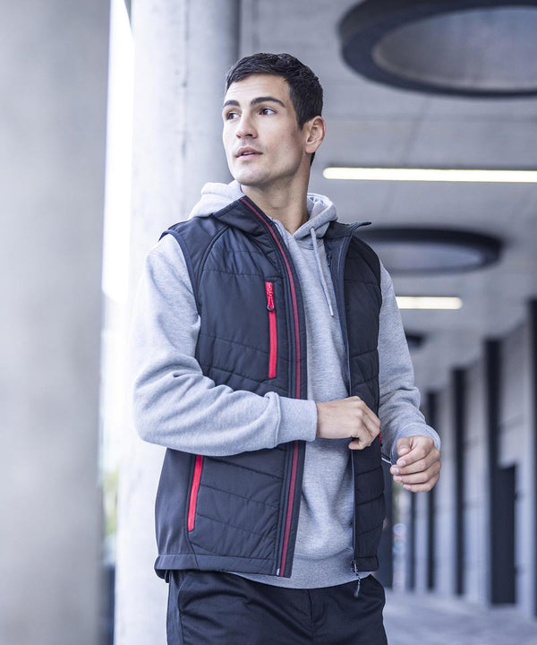 A man wearing a grey hoodie and a Regatta Professional Pro universal bodywarmer stands outside by concrete pillars and circular ceiling lights, looking to the side.