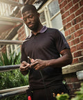 A man in a dark polo shirt stands outside a brick building, handling electrical wires with a focused expression. Various tools are visible in his pocket, including the RG663 from Regatta.