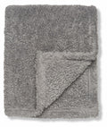 A folded, fluffy blanket named RI010 by Ribbon, showcasing a turned-over corner on a gray surface.