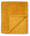 A folded, plush Ribbon RI010 blanket in mustard yellow with one corner flipped to reveal its soft texture.