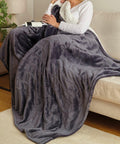 Person sitting on a sofa, wrapped in a plush gray blanket, and holding a white Ribbon RI012.
