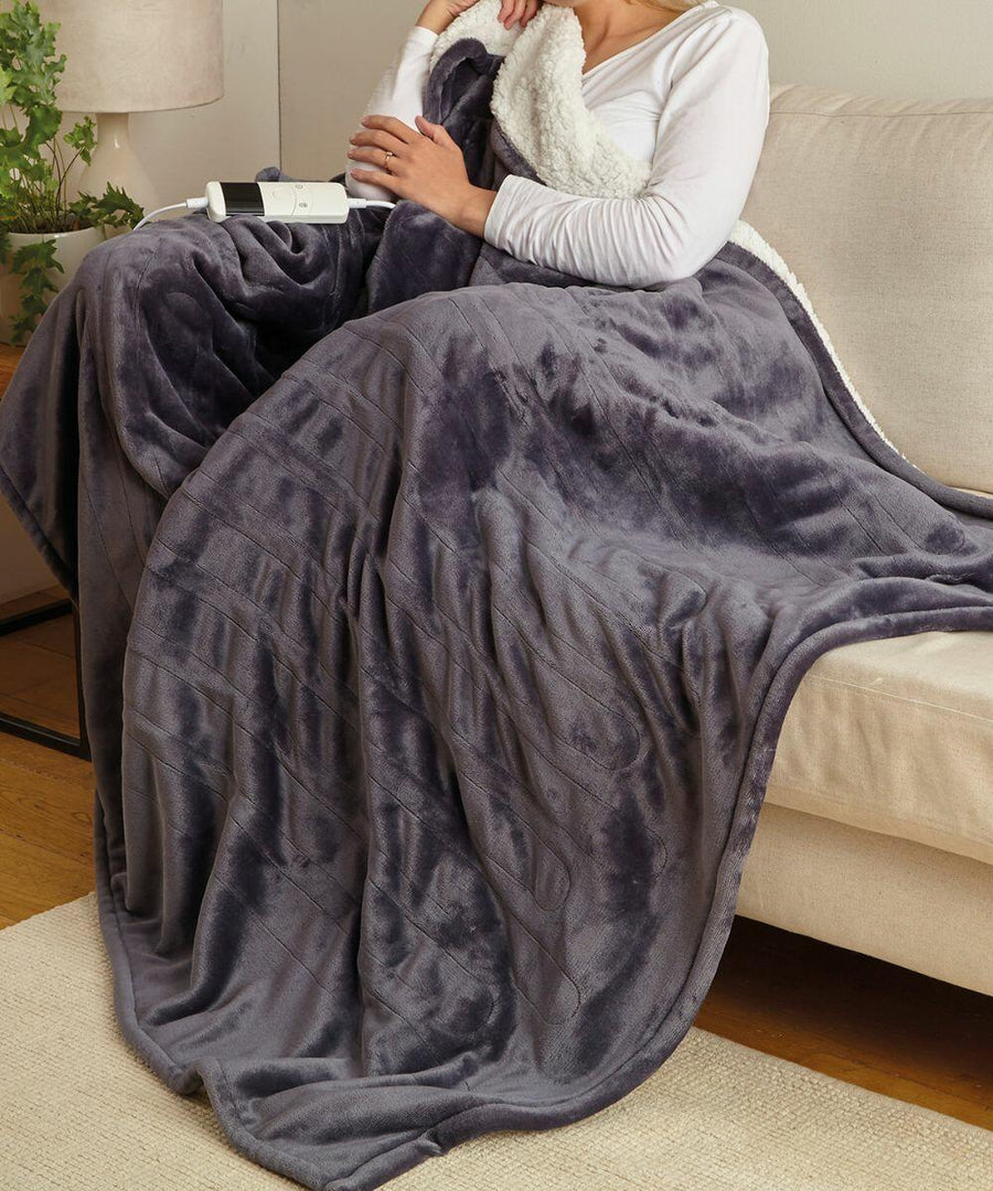 Person sitting on a sofa, wrapped in a plush gray blanket, and holding a white Ribbon RI012.